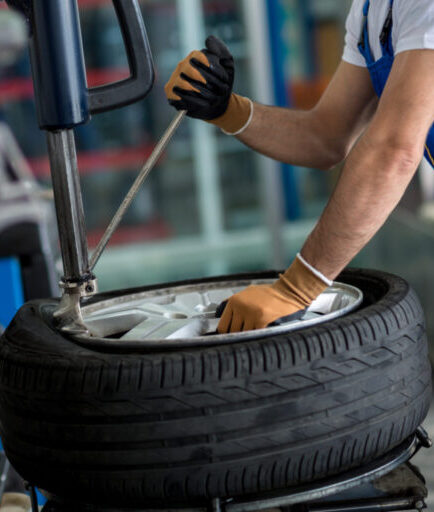 Man using tyre tools and machine to fit it on the wheel.